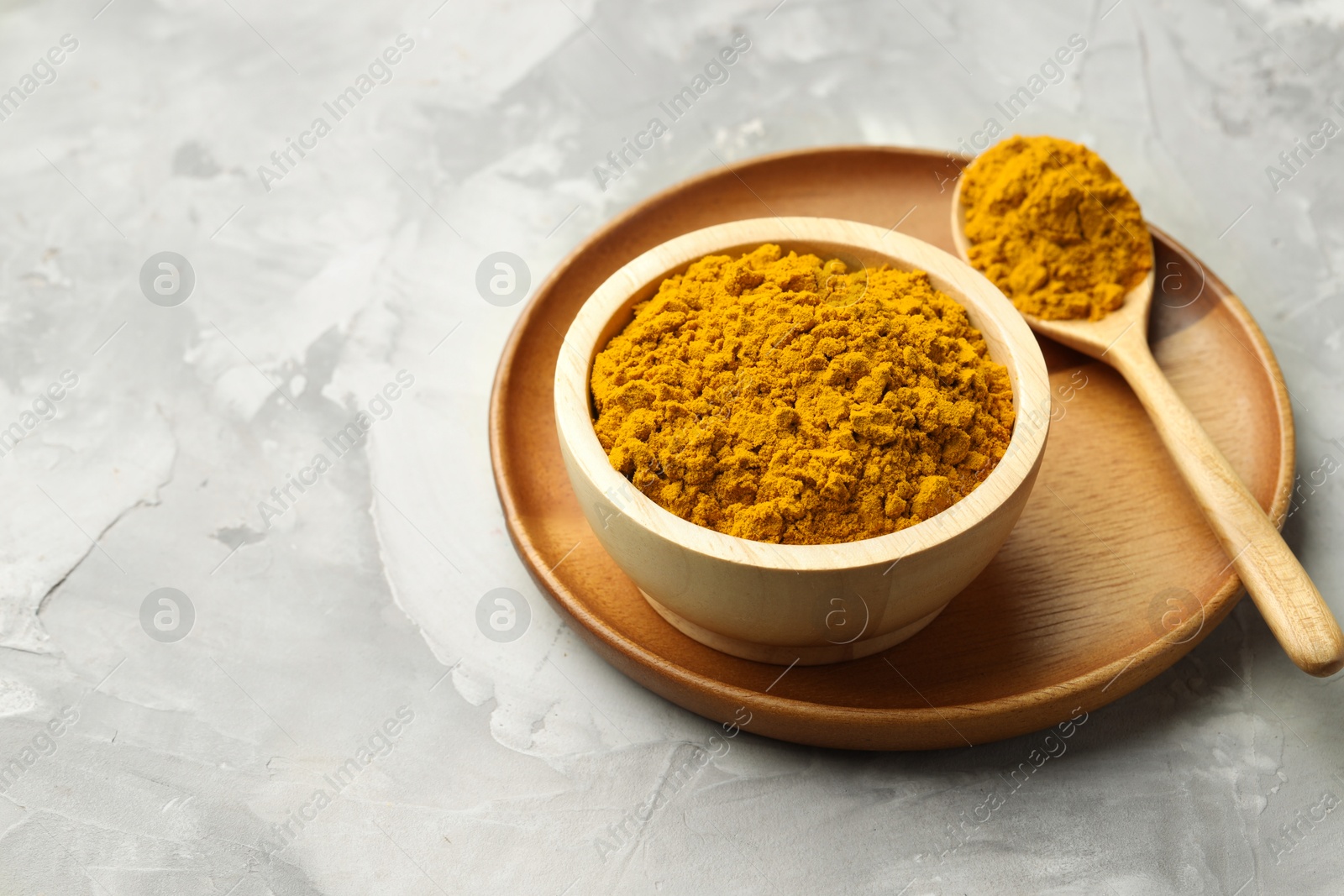 Photo of Turmeric powder in bowl and spoon on light grey table, space for text