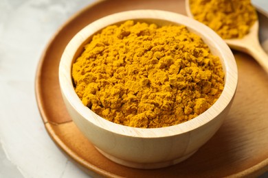 Photo of Turmeric powder in bowl on light table, closeup