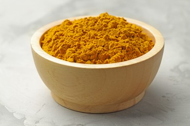 Photo of Turmeric powder in bowl on light table, closeup