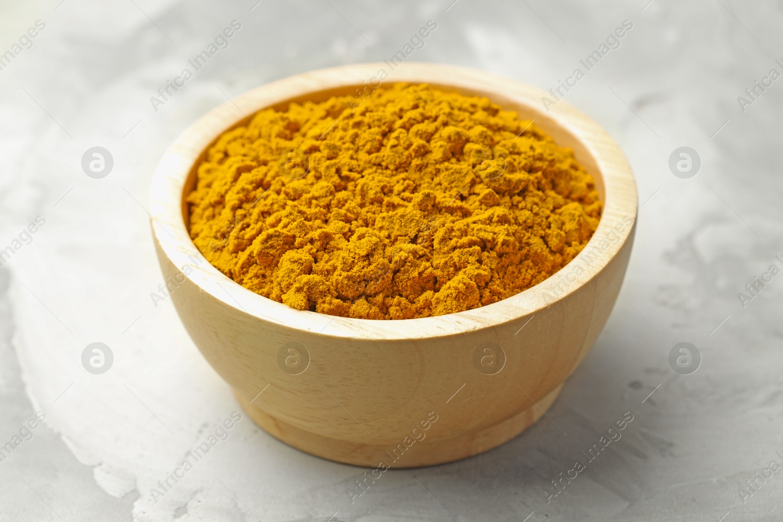 Photo of Turmeric powder in bowl on light table, closeup