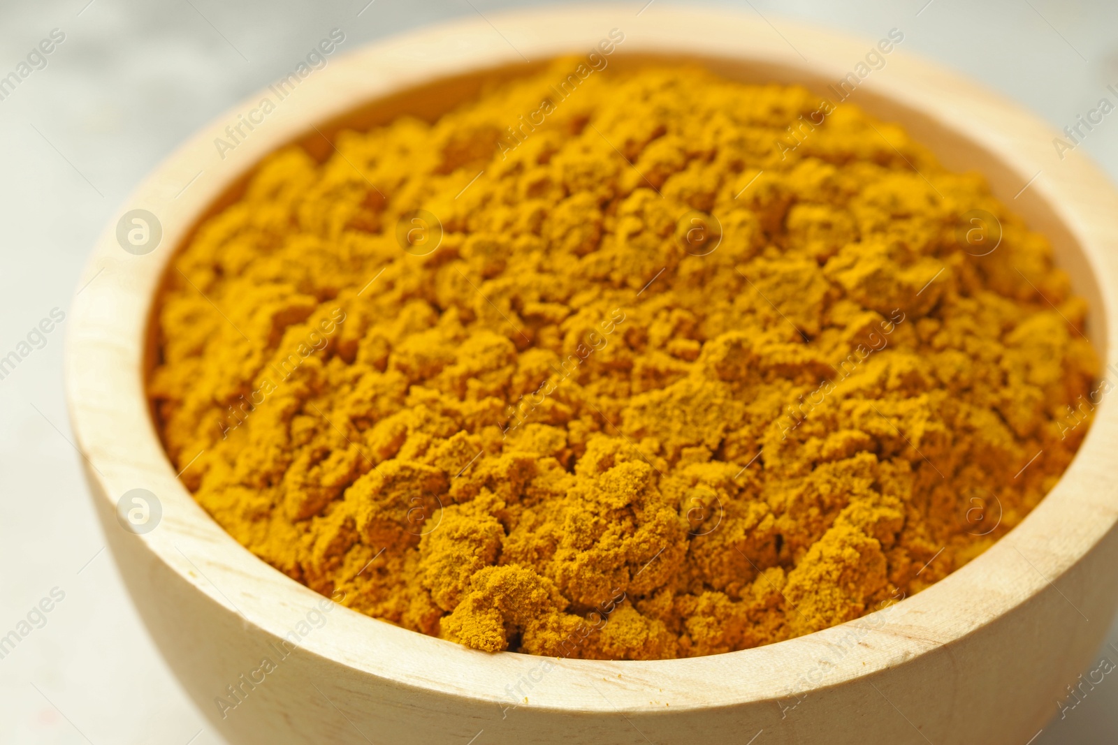 Photo of Turmeric powder in bowl on light table, closeup