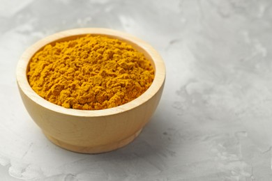 Photo of Turmeric powder in bowl on light grey table, closeup. Space for text