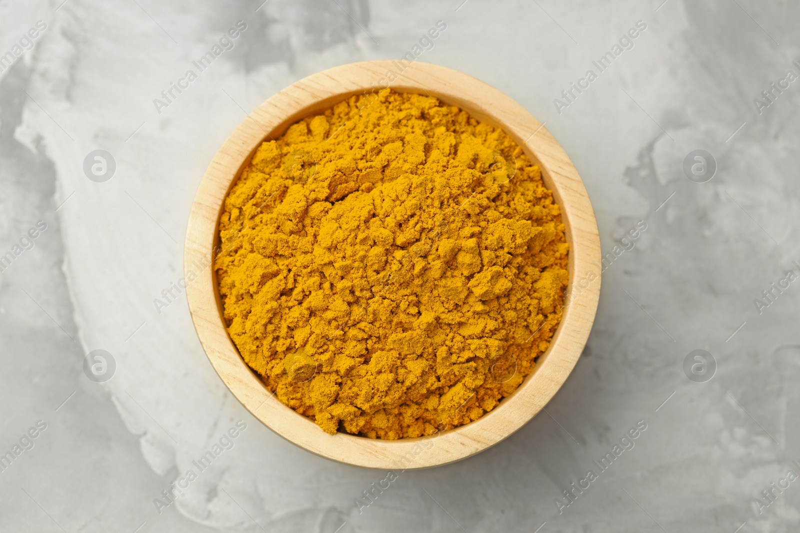 Photo of Turmeric powder in bowl on light grey table, top view