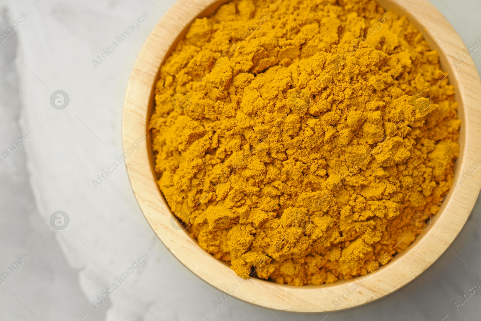 Photo of Turmeric powder in bowl on light grey table, top view