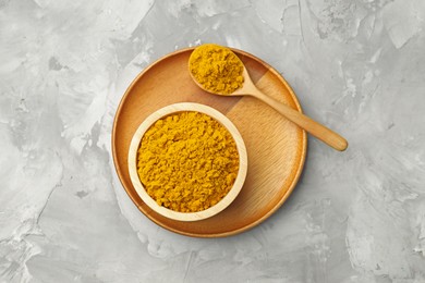 Photo of Turmeric powder in bowl and spoon on light grey table, top view