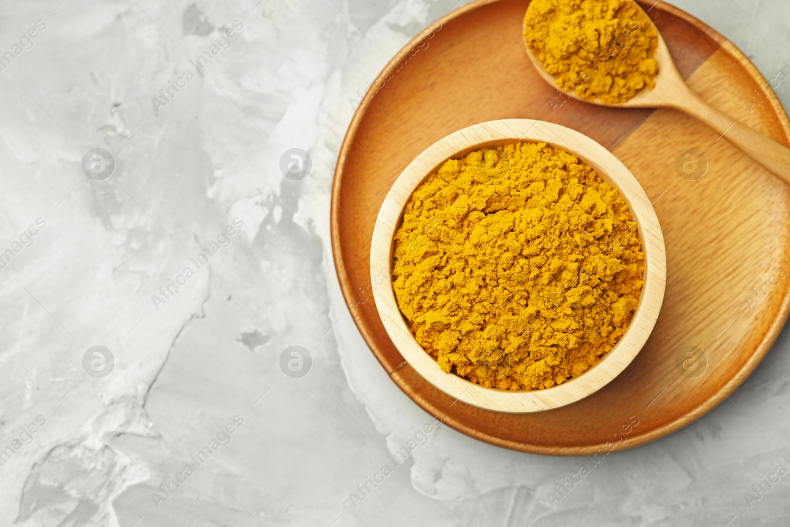 Photo of Turmeric powder in bowl and spoon on light grey table, top view. Space for text