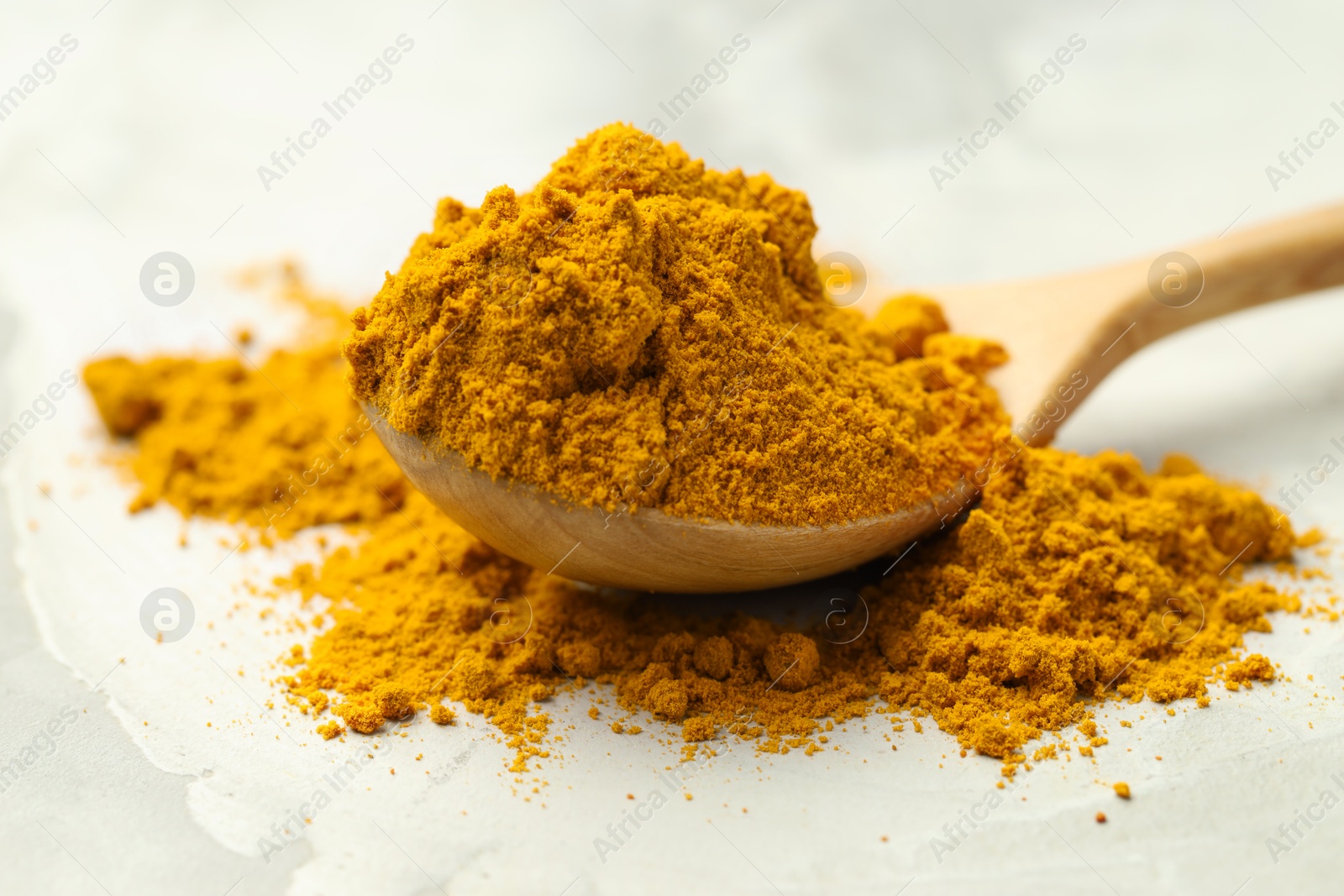 Photo of Turmeric powder and spoon on light grey table, closeup