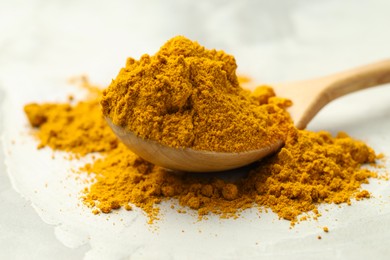 Photo of Turmeric powder and spoon on light grey table, closeup