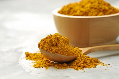 Photo of Turmeric powder and spoon on light grey table, closeup