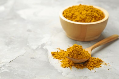 Photo of Turmeric powder in spoon and bowl on light grey table, closeup. Space for text