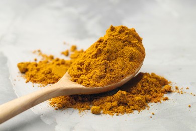 Photo of Turmeric powder and spoon on light grey table, closeup