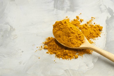 Photo of Turmeric powder and spoon on light grey table, closeup. Space for text