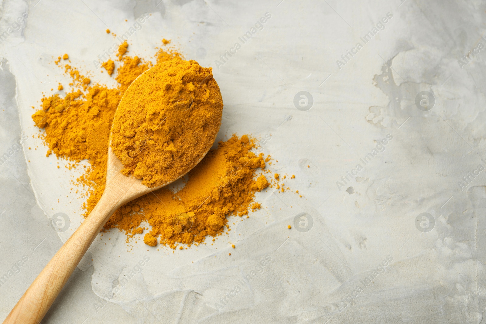 Photo of Turmeric powder and spoon on light grey table, top view. Space for text