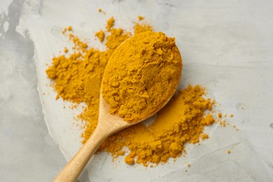 Photo of Turmeric powder and spoon on light grey table, top view