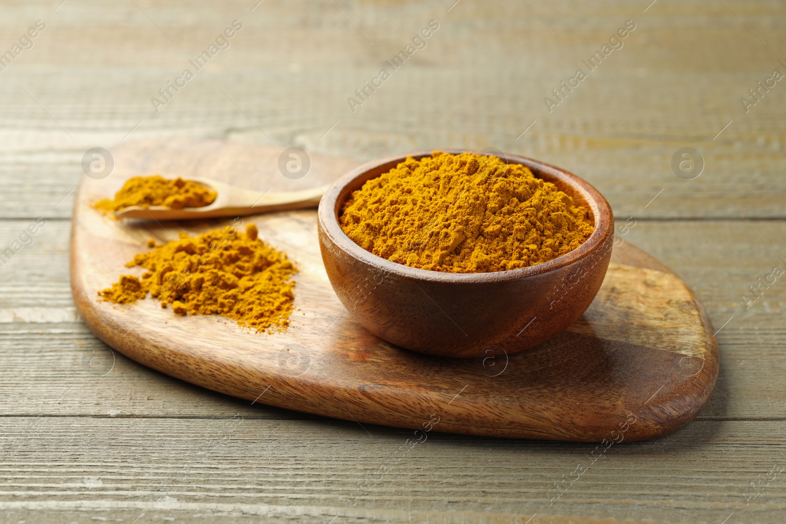 Photo of Turmeric powder in bowl and spoon on wooden table, closeup