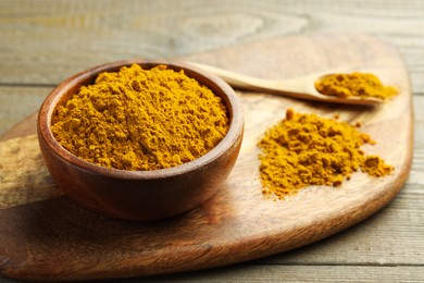 Photo of Turmeric powder in bowl and spoon on wooden table, closeup