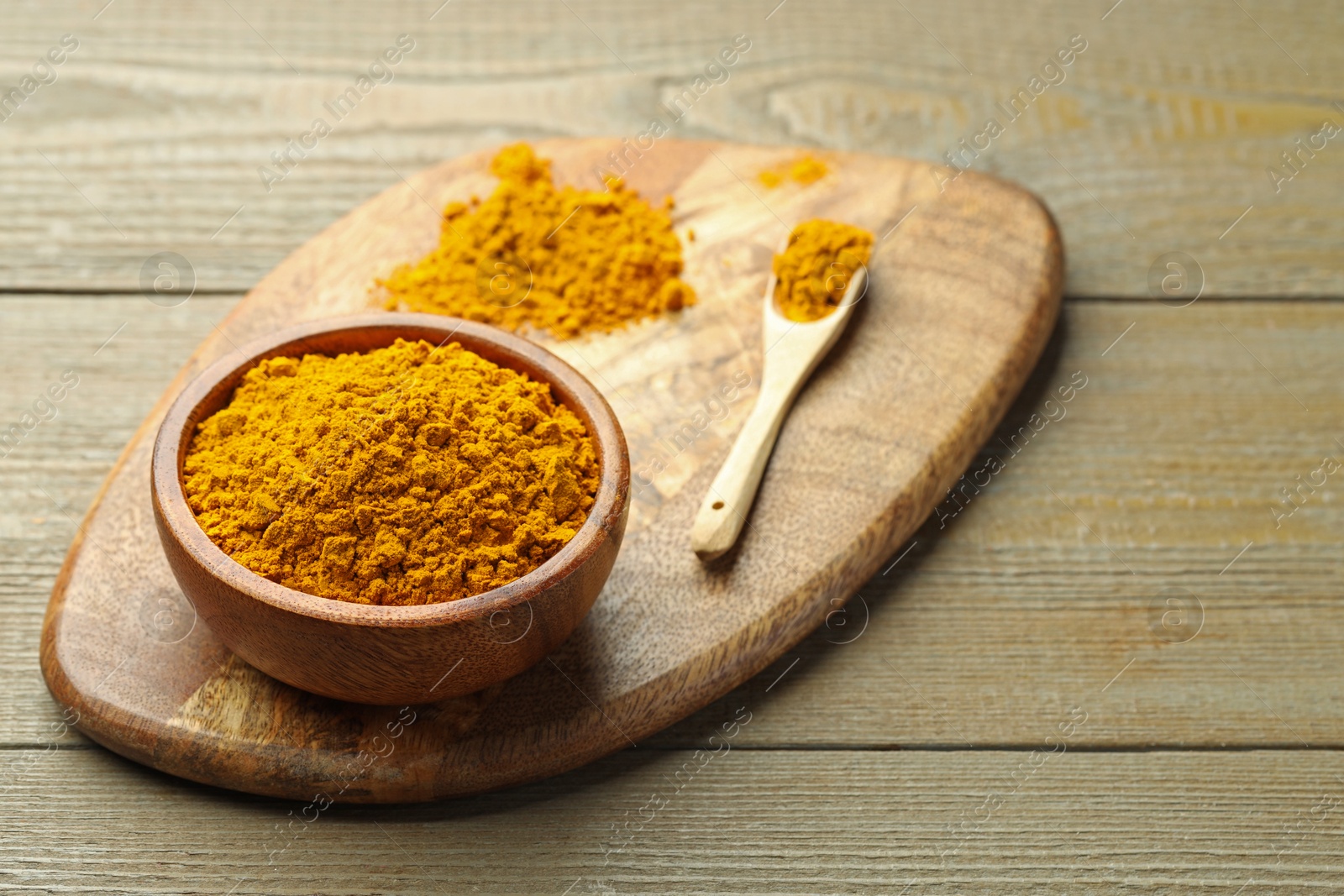 Photo of Turmeric powder in bowl and spoon on wooden table, closeup