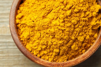 Photo of Turmeric powder in bowl on wooden table, top view