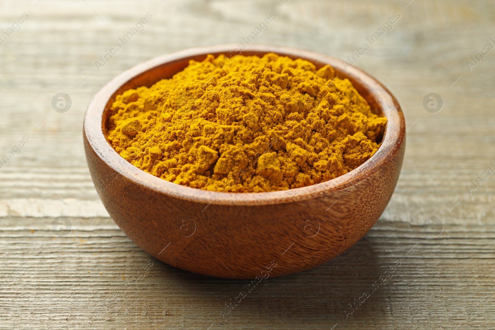 Photo of Turmeric powder in bowl on wooden table, closeup