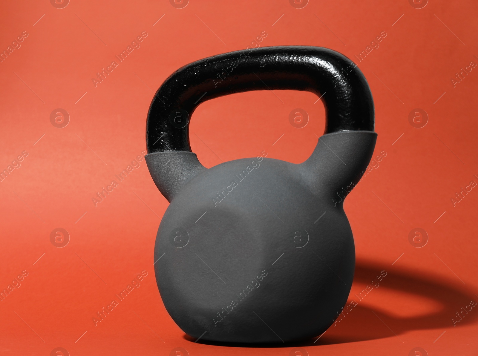 Photo of One metal kettlebell on coral background, closeup. Sports equipment