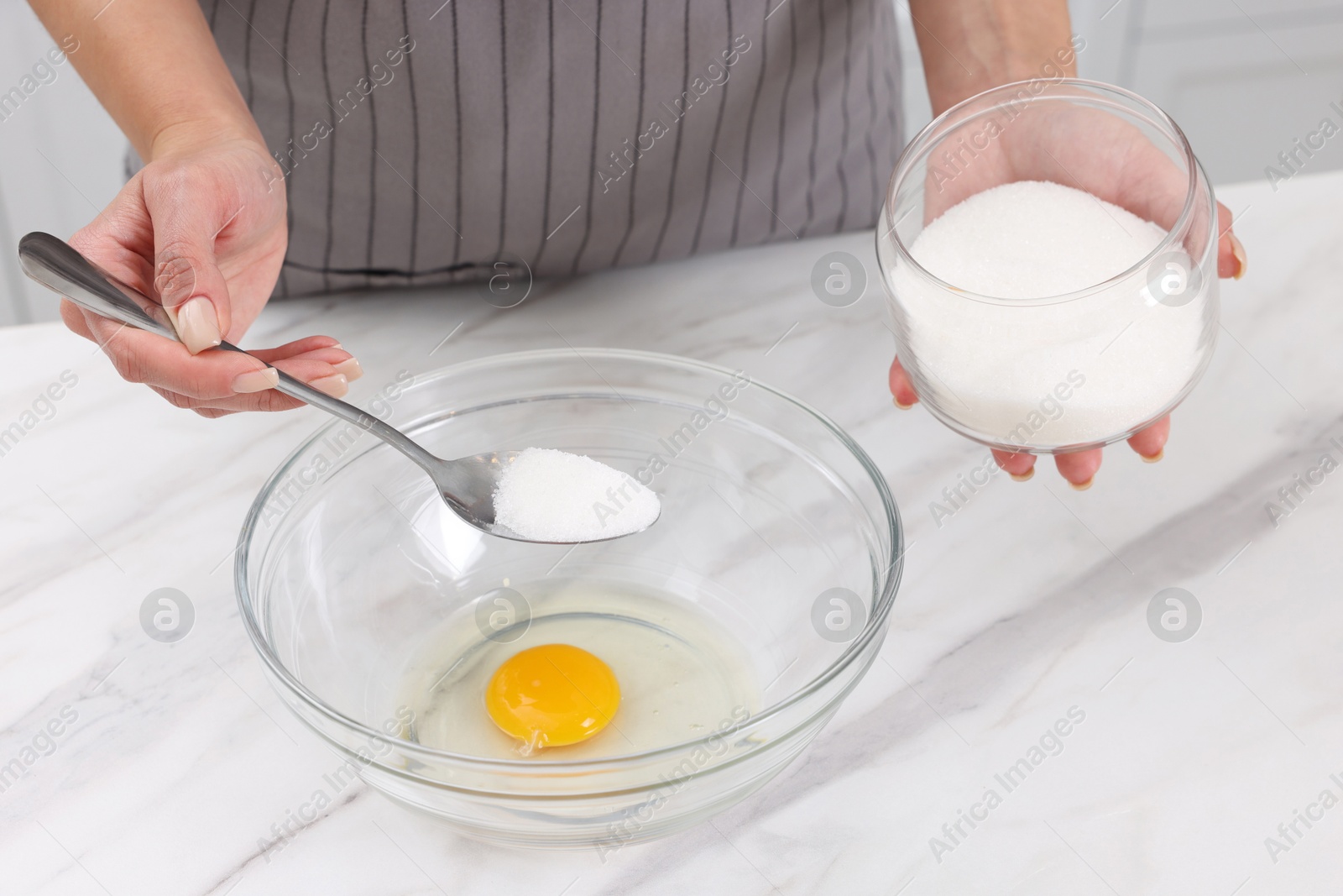 Photo of Making dough. Woman adding sugar into bowl with egg at white marble table, closeup