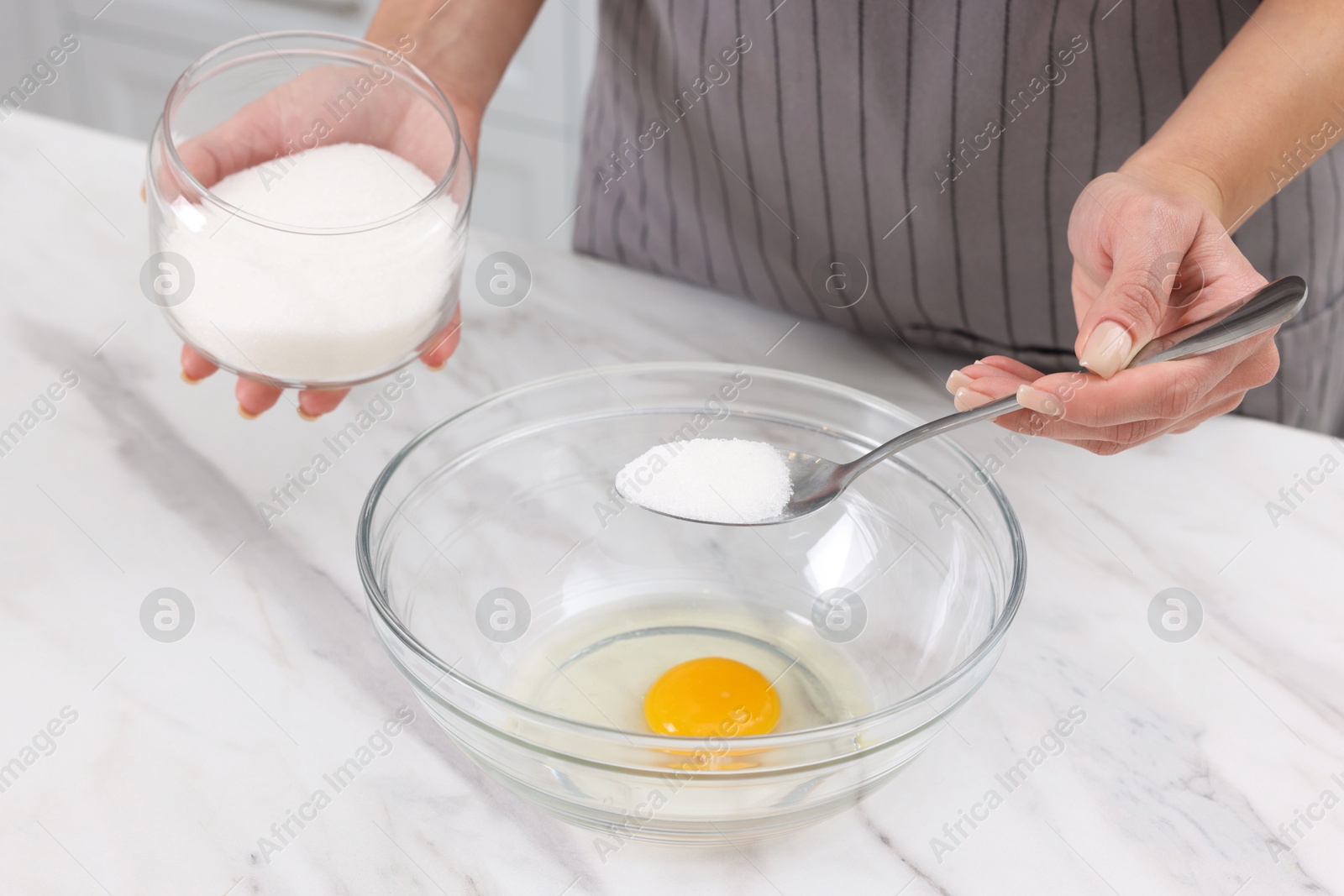 Photo of Making dough. Woman adding sugar into bowl with egg at white marble table, closeup