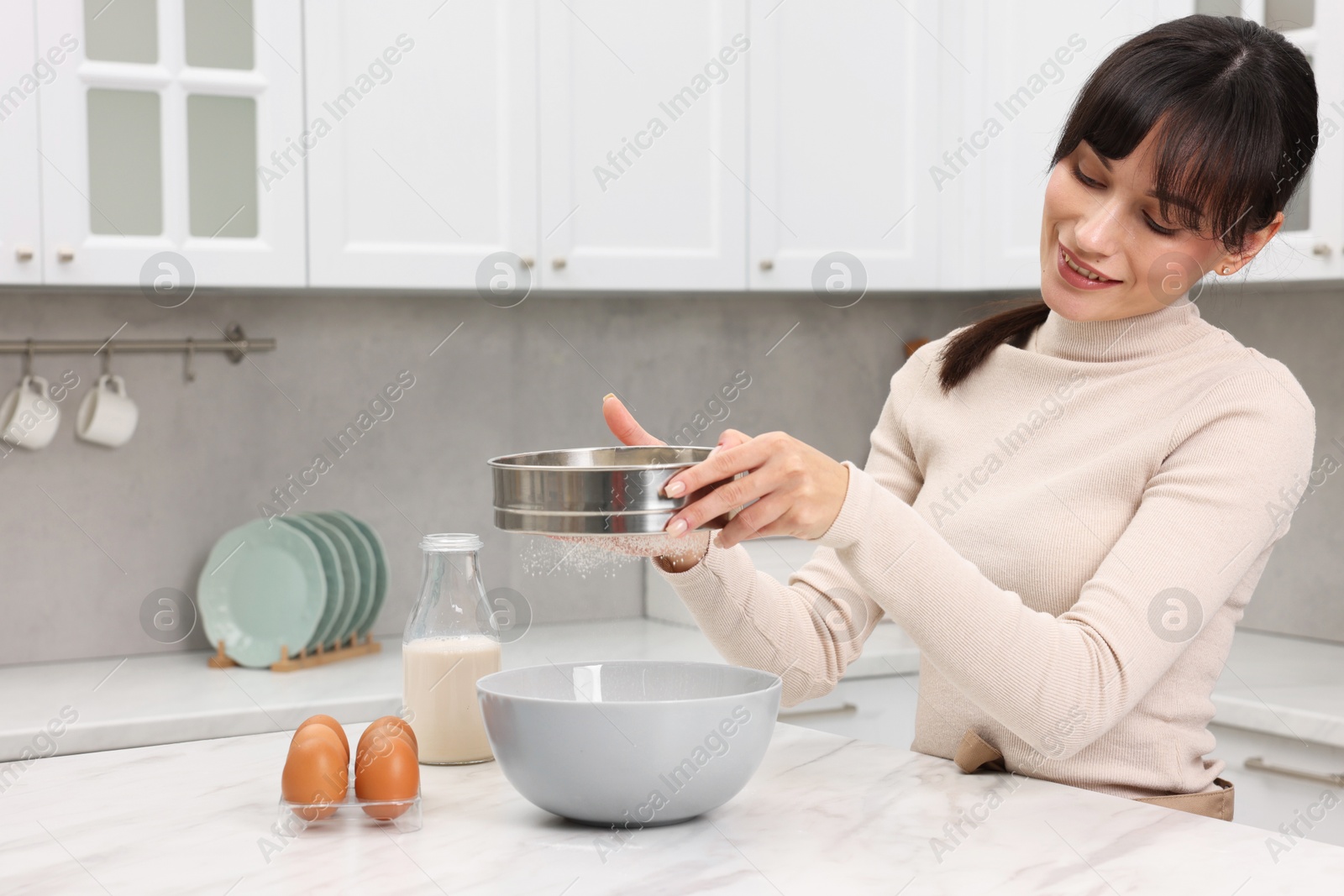 Photo of Making dough. Woman sifting flour into bowl at white table. Space for text