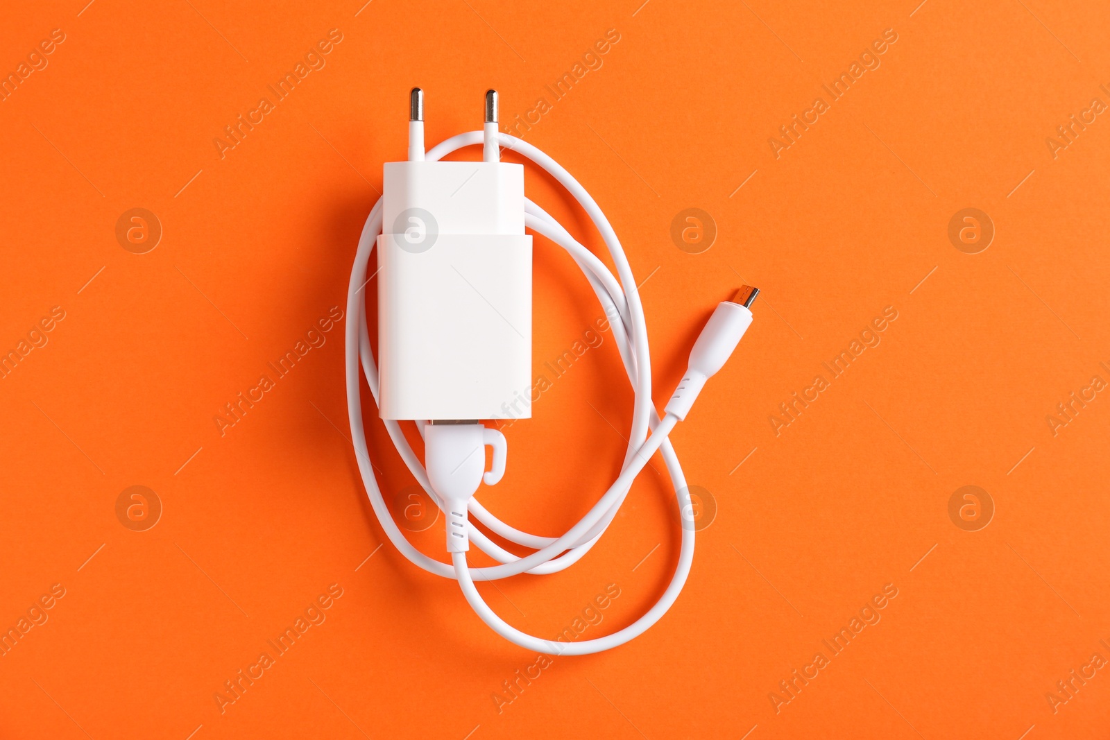 Photo of USB power adapter with charge cable on orange background, top view