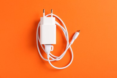 Photo of USB power adapter with charge cable on orange background, top view