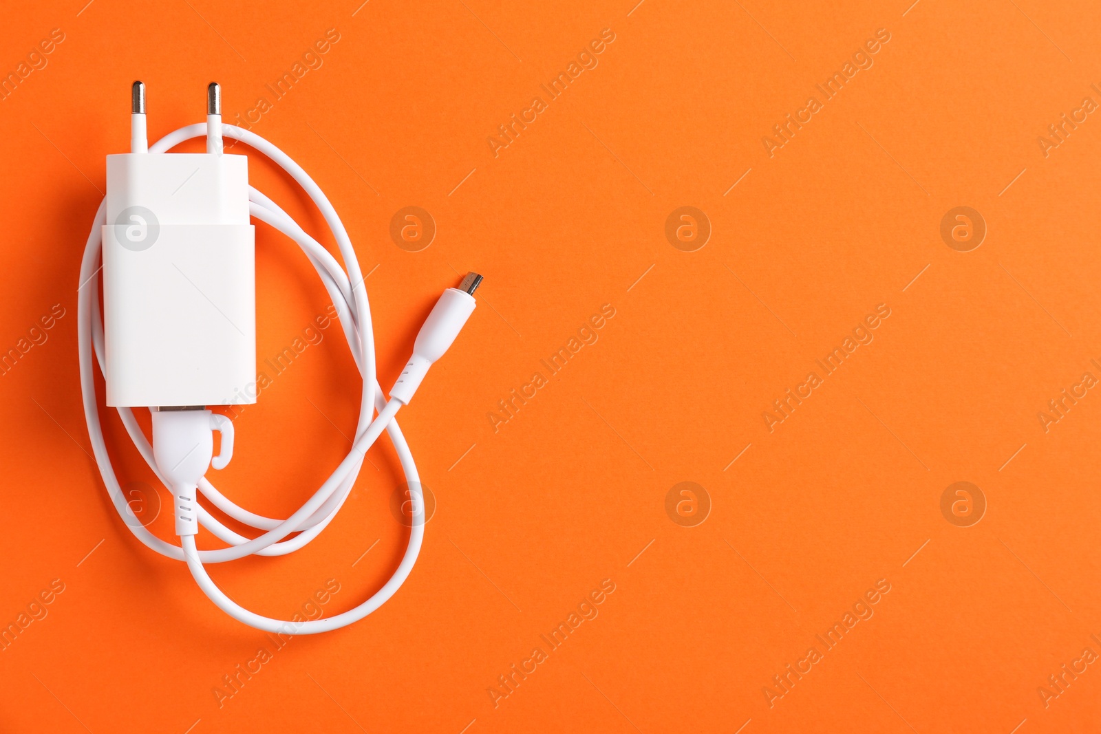 Photo of USB power adapter with charge cable on orange background, top view. Space for text