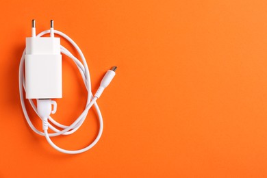 Photo of USB power adapter with charge cable on orange background, top view. Space for text