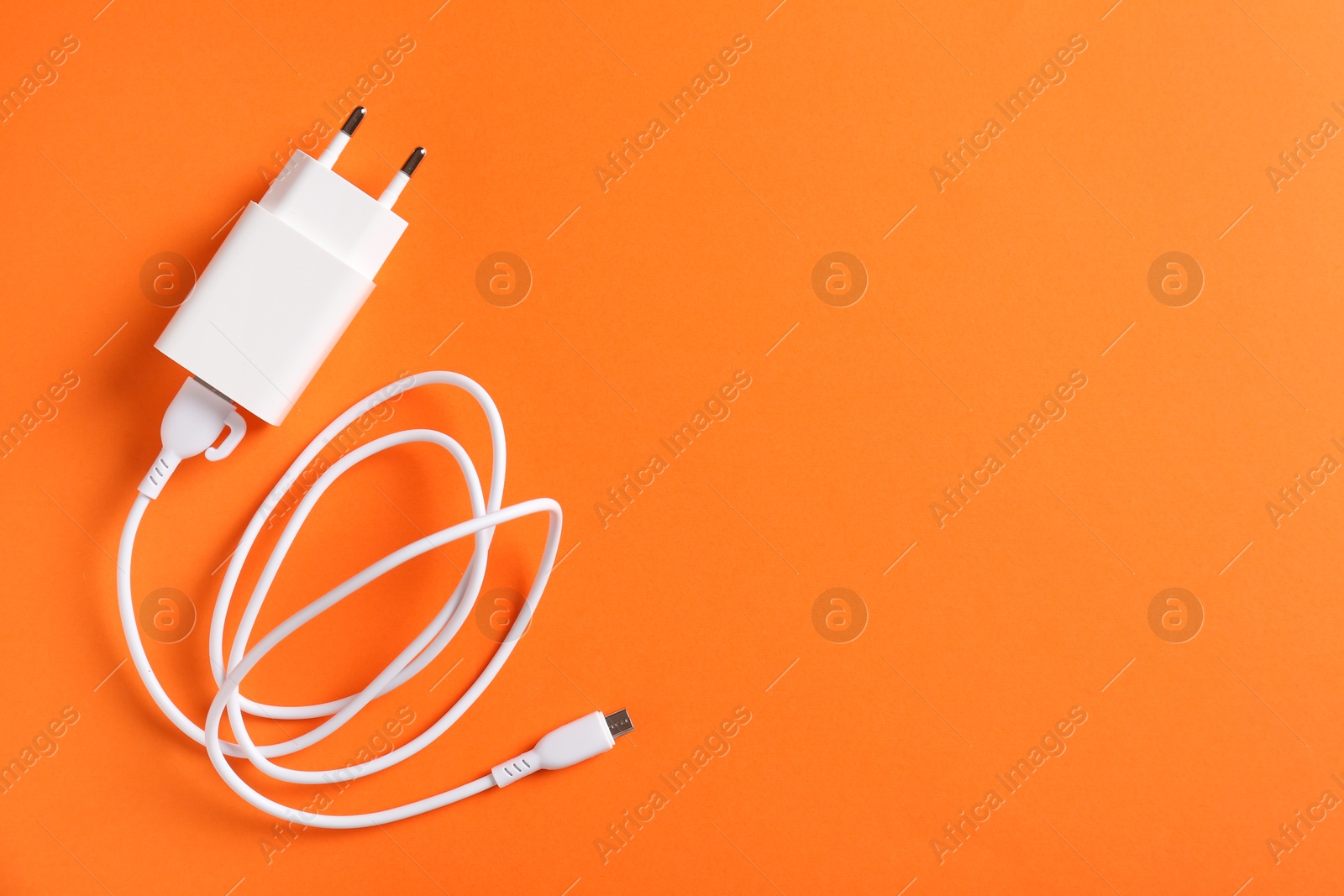 Photo of USB power adapter with charge cable on orange background, top view. Space for text