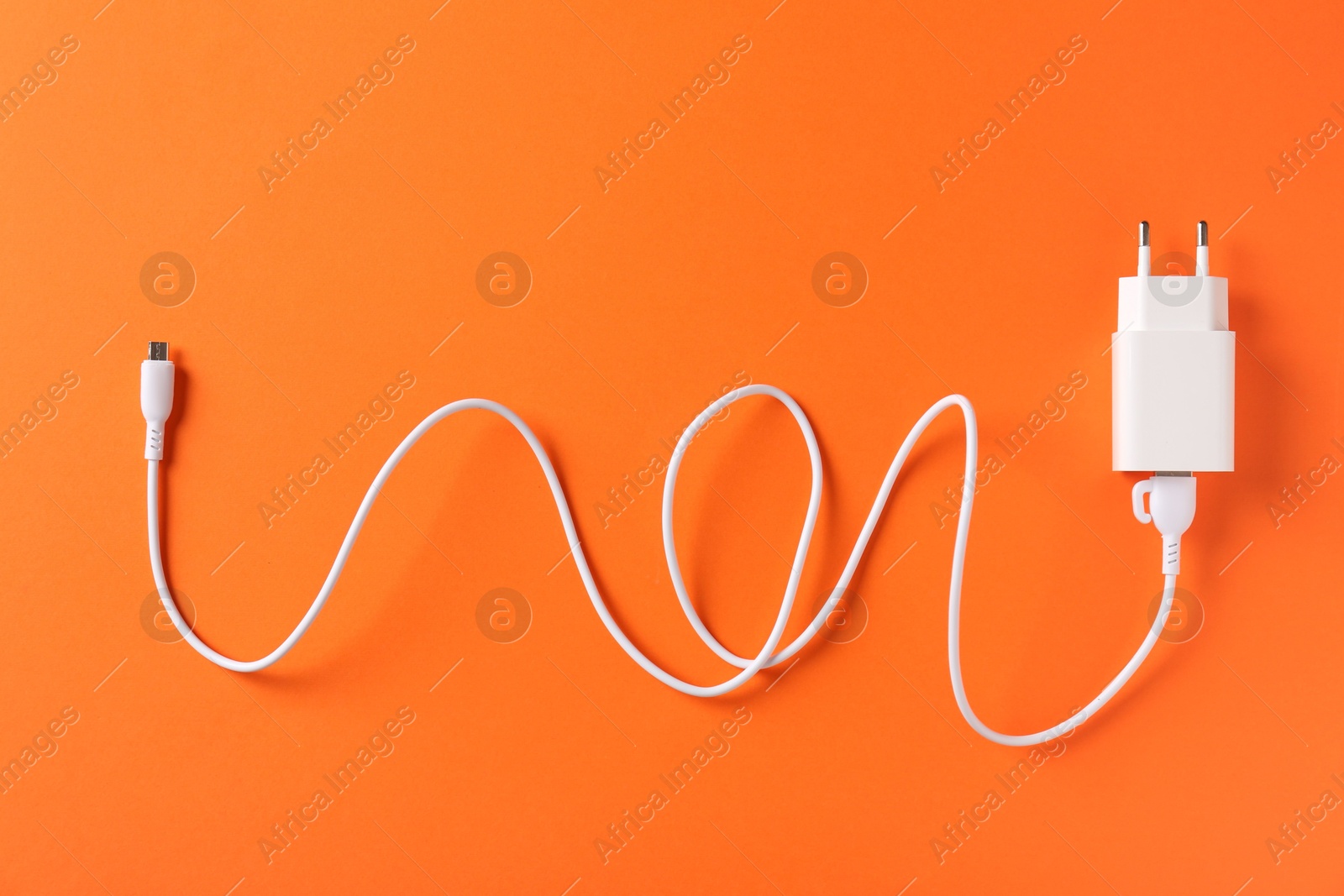 Photo of USB power adapter with charge cable on orange background, top view