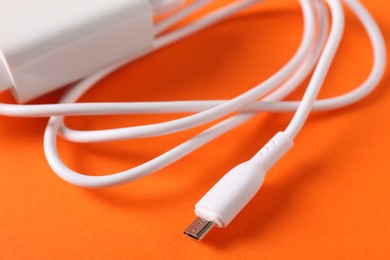 Photo of USB power adapter with charge cable on orange background, closeup