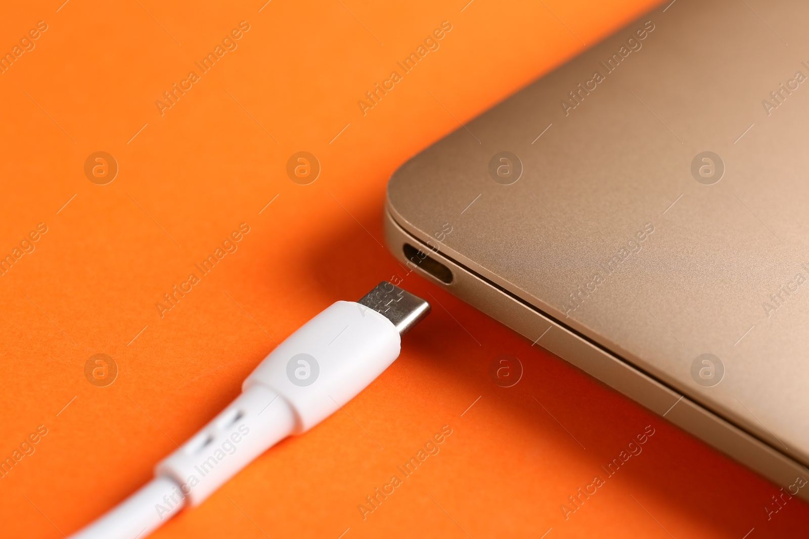 Photo of USB charge cable with lightning connector and laptop on orange background, closeup