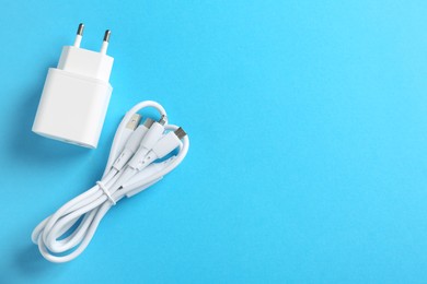 Photo of USB power adapter and triple charge cable on light blue background, flat lay. Space for text