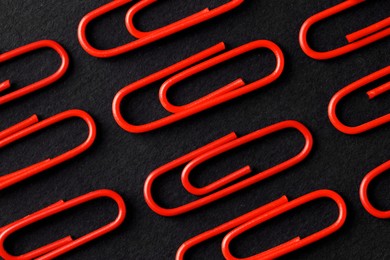 Photo of Red paper clips on black background, flat lay