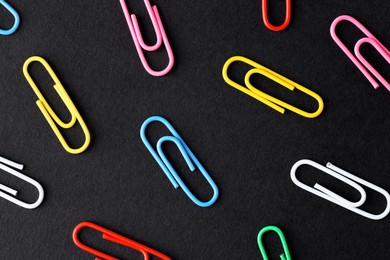 Colorful paper clips on black background, flat lay