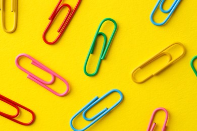 Colorful paper clips on yellow background, flat lay