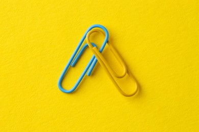 Photo of Two paper clips on yellow background, top view