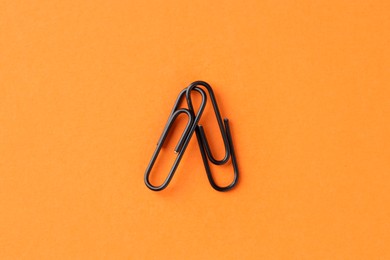 Photo of Two paper clips on orange background, top view