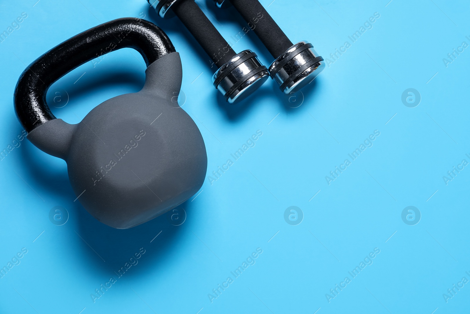 Photo of Kettlebell and dumbbells on light blue background, flat lay. Space for text