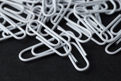 Photo of Many white paper clips on black table, closeup