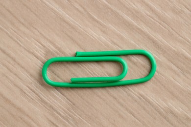 One green paper clip on wooden table, top view