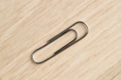 One metal paper clip on wooden table, top view