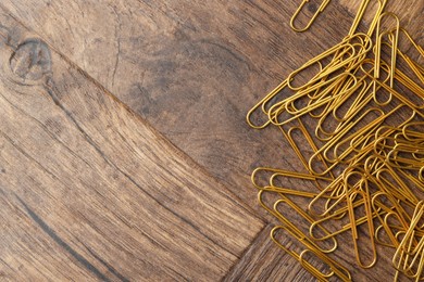 Photo of Many golden paper clips on wooden table, top view. Space for text