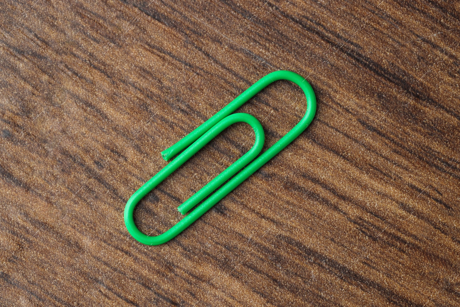 Photo of One green paper clip on wooden table, top view