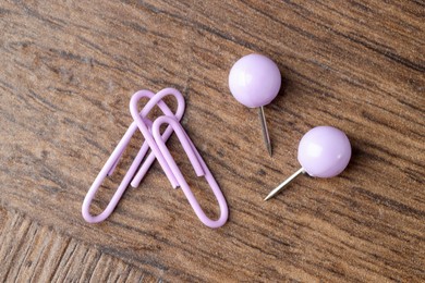 Two violet paper clips and pins on wooden table, flat lay