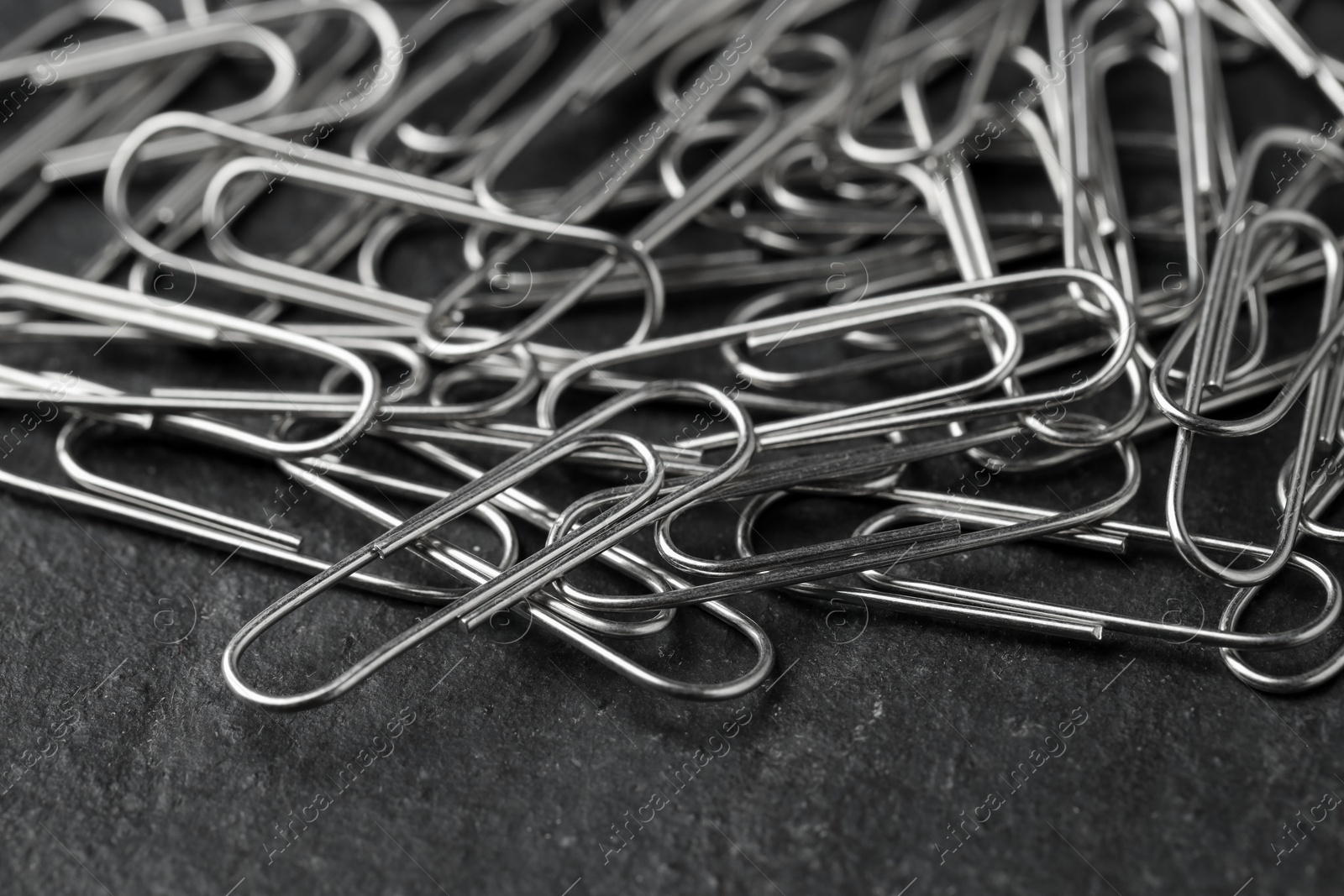 Photo of Many metal paper clips on black table, closeup