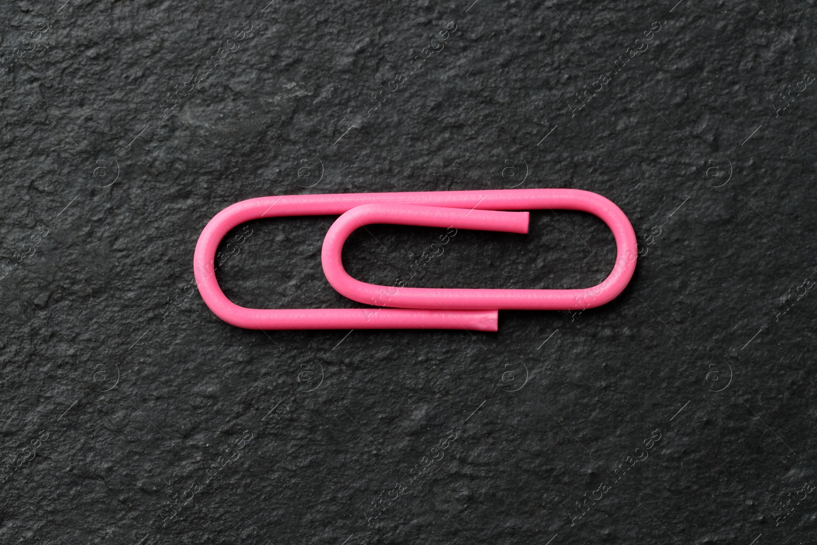 Photo of One pink paper clip on black table, top view